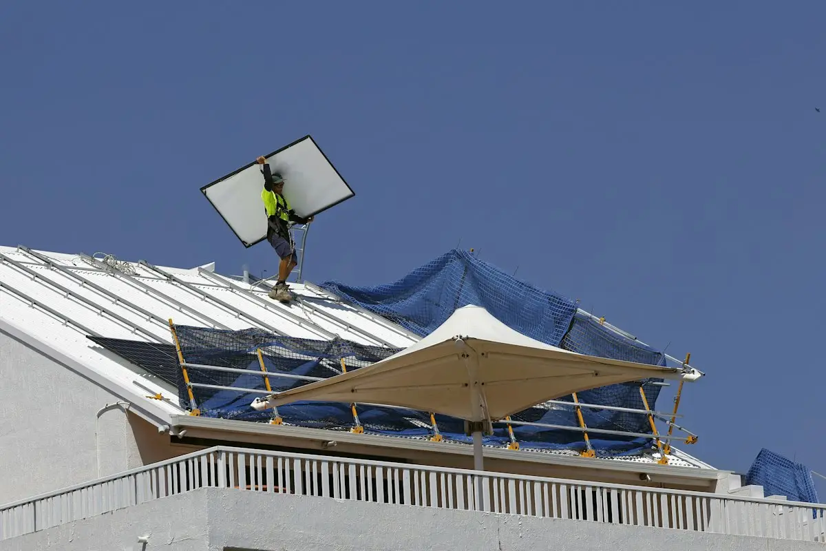 Solar installer carrying a panel across a sunny rooftop